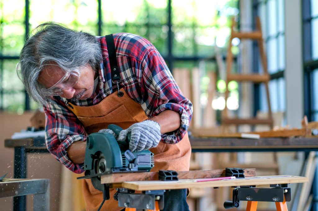 Asian senior craftsman use electrical saw to cut wood and generate wood dust